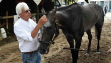 Bob Baffert, wearing a white button-down shirt and jeans, stands in his barn area at Saratoga Race Course, holding the gray/roan horse Arrogate and toying with the horse's forelock