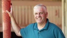 Trainer Bruce Brown, wearing a teal shirt, stands in the saddling enclosure at Saratoga Race Course