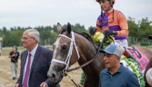 Ned Toffey leads Ted Noffey, his spoonerism namesake and a gray/road horse, into the winner's circle at Saratoga Race Course. Riding Ted Noffey is John Velazquez, wearing silks with purple and orange squares.